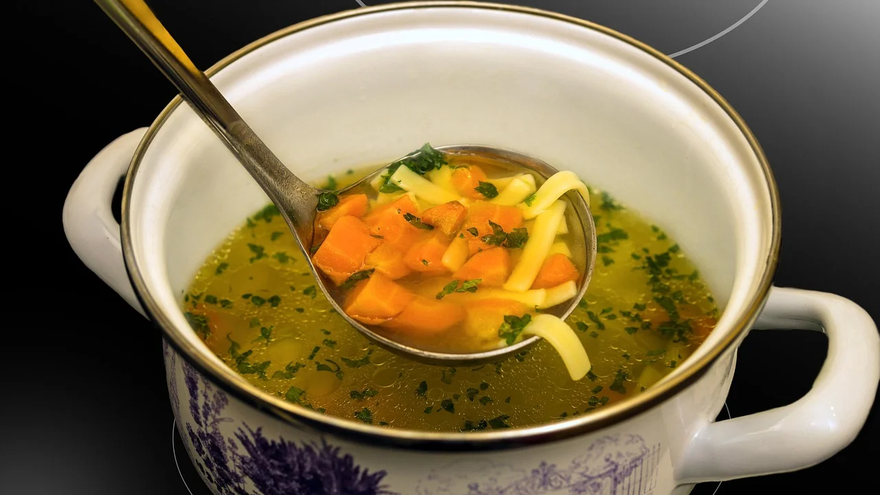 Caldo límpido servido com ervas frescas em tigela.