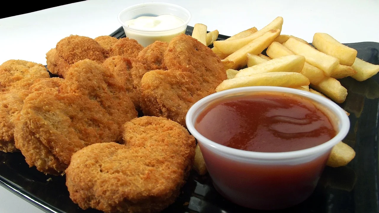 Porção de nuggets crocantes servida com molho cremoso e vegetais frescos.
