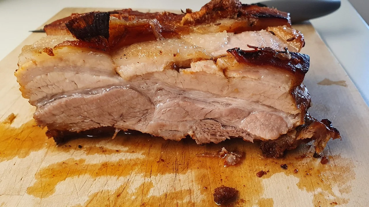 Pernil suíno dourado em assadeira com ervas frescas.