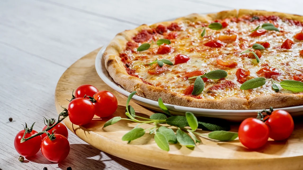 Massa de pizza aberta em disco pequeno sobre bancada enfarinhada.