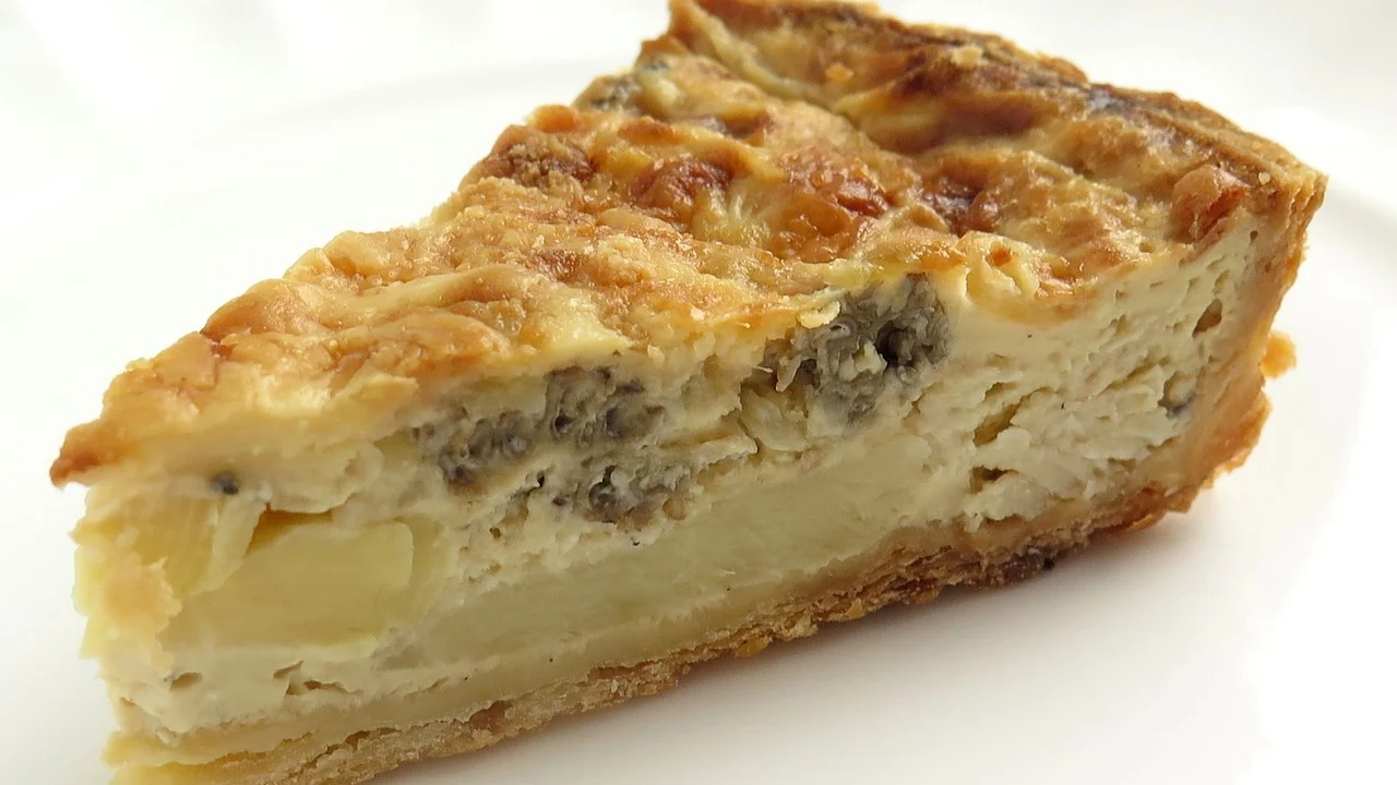 Quiche de queijo dourada em forma redonda sobre a mesa