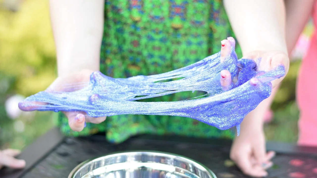Mãos misturam cola colorida para formar slime caseiro.