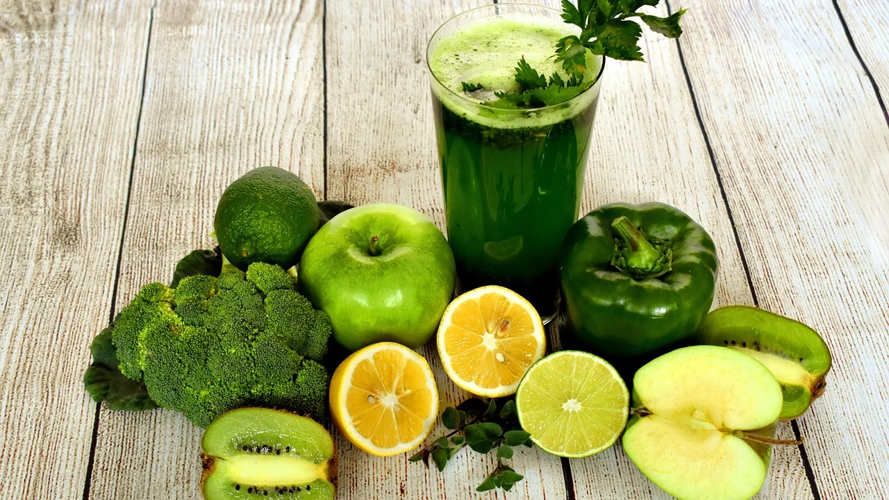 Suco verde servido em copo de vidro com folhas frescas ao lado.